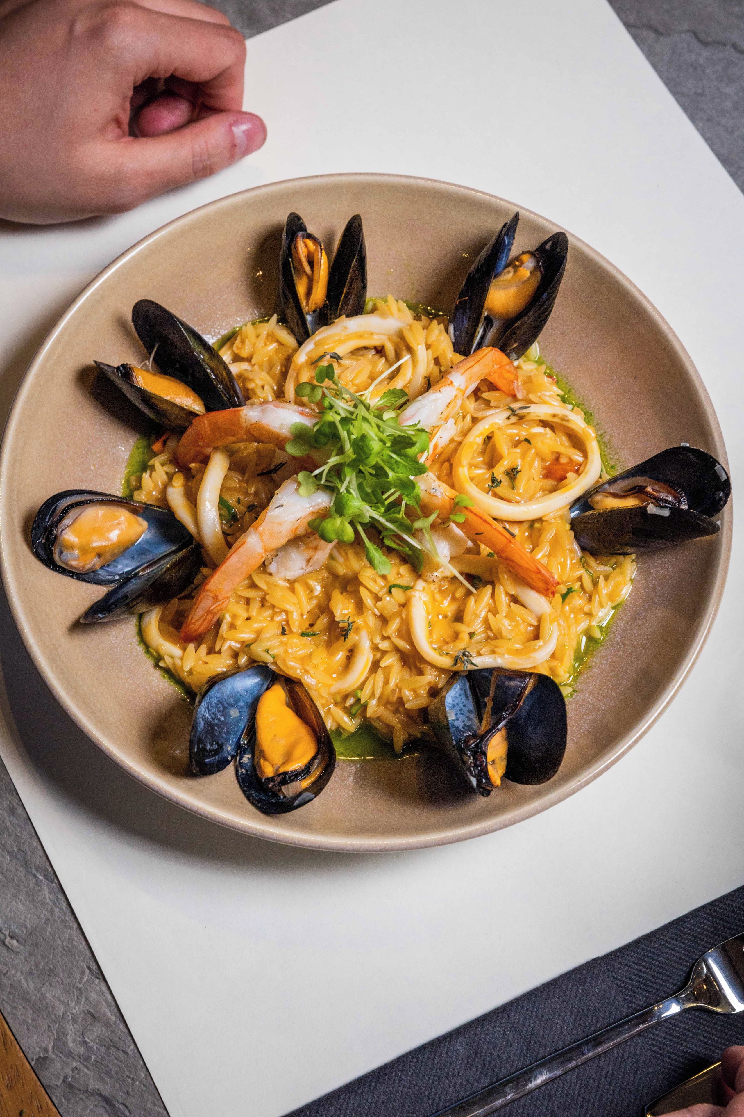 Une assiette de pâtes aux fruits de mer, avec des moules et des crevettes, garnie de verdure.