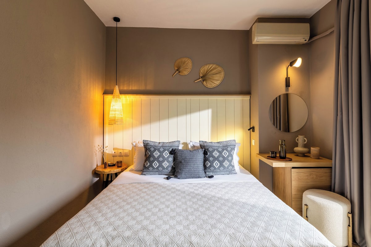 A neatly arranged hotel room with a bed, bedside table, lamp, and a small desk with a mirror.