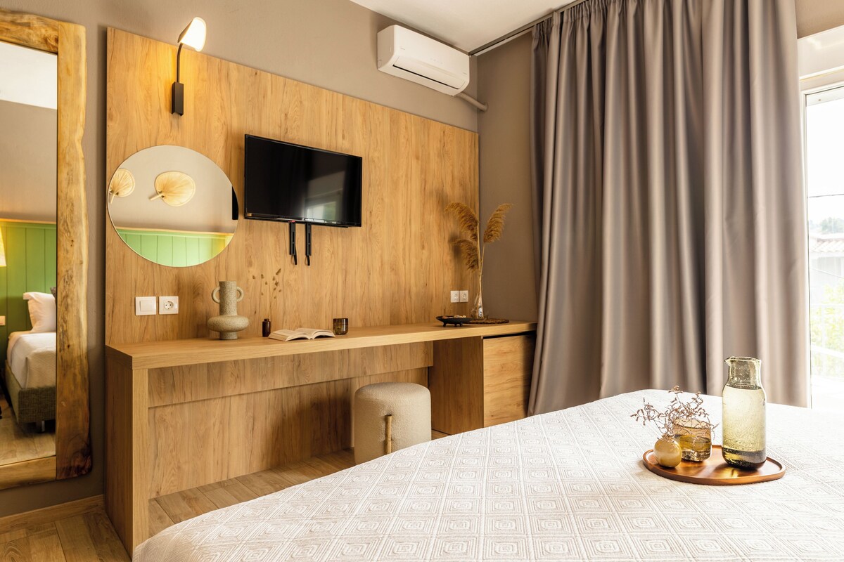 A hotel room with a wooden vanity, a mounted TV, a bed with a patterned bedspread, and a window with curtains.
