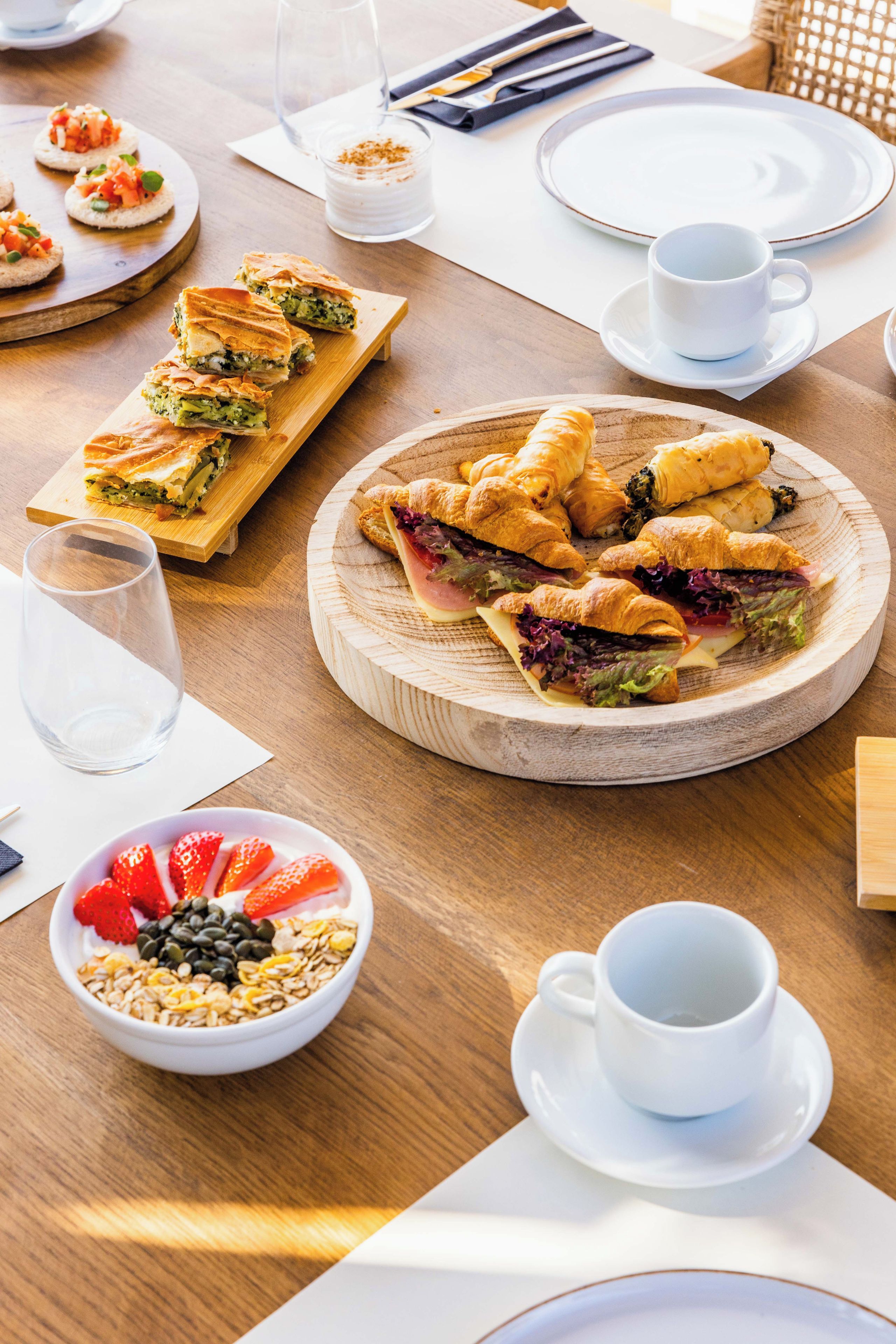 Desayuno con bollería, sándwiches y un bol de fruta y granola.
