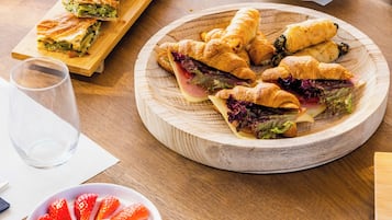 Ein Frühstücksbuffet mit Gebäck, Sandwiches und einer Schüssel Obst und Granola.