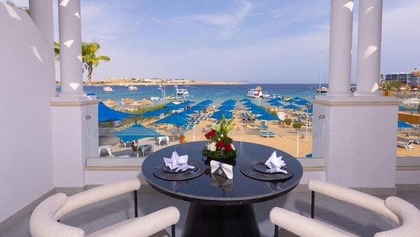 A table with a view of a beach and boats, surrounded by white columns and blue umbrellas. - Naama Bay Suites & Spa - Sharm (Sharm El Sheikh)