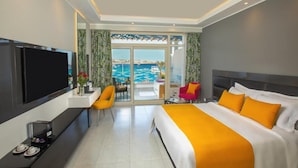 A modern hotel room with a large bed, a flat-screen TV, a desk with a coffee maker, and a view of the sea through a glass door. - Naama Bay Suites & Spa - Sharm (Sharm El Sheikh)