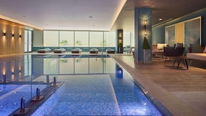 A modern indoor pool area with glass railings, seating by the pool, and a view of the outdoors through large windows. - Radisson Blu Hotel Riyadh Convention & Exhibition Center (Riyadh)