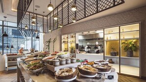 A buffet setup with various food items and a kitchen area visible through a glass partition. - Radisson Blu Hotel Riyadh Convention & Exhibition Center (Riyadh)
