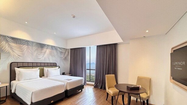Habitación de hotel con dos camas, una mesa de comedor con sillas, vistas al exterior y un cartel en la pared.
