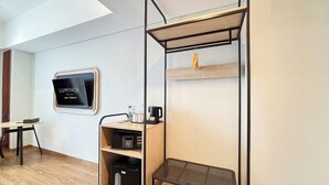 Una habitación de hotel moderna con cama, televisor, máquina de café y zapatero.