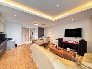 A modern living room with a sofa, a dining area, a kitchen, and a TV displaying "LUMINOR HOTEL". - Luminor Hotel Padjadjaran Bogor (Bogor)