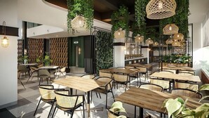 A modern restaurant interior with wooden tables and chairs, hanging plants, and wicker pendant lights.