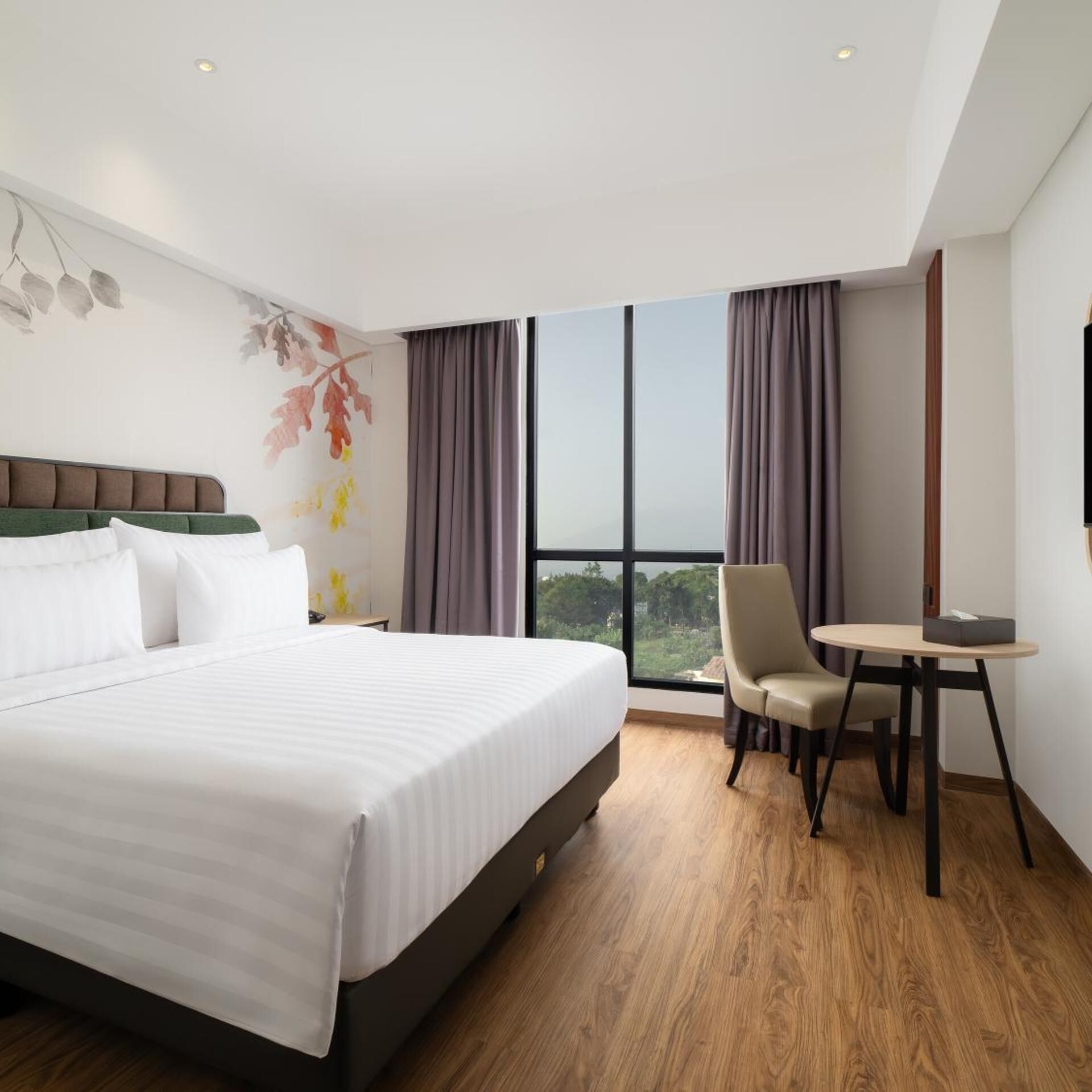 A hotel room with a large bed, a desk, and a chair, a window with curtains, and a wall with a leaf pattern.