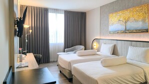 Habitación de hotel con dos camas, un escritorio, una silla, un cuadro y una ventana con cortinas.