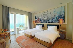 Ein Hotelzimmer mit zwei Betten, einem Esstisch, einem Balkon mit Vorhängen und einem großen Wandbild im tropischen Stil.