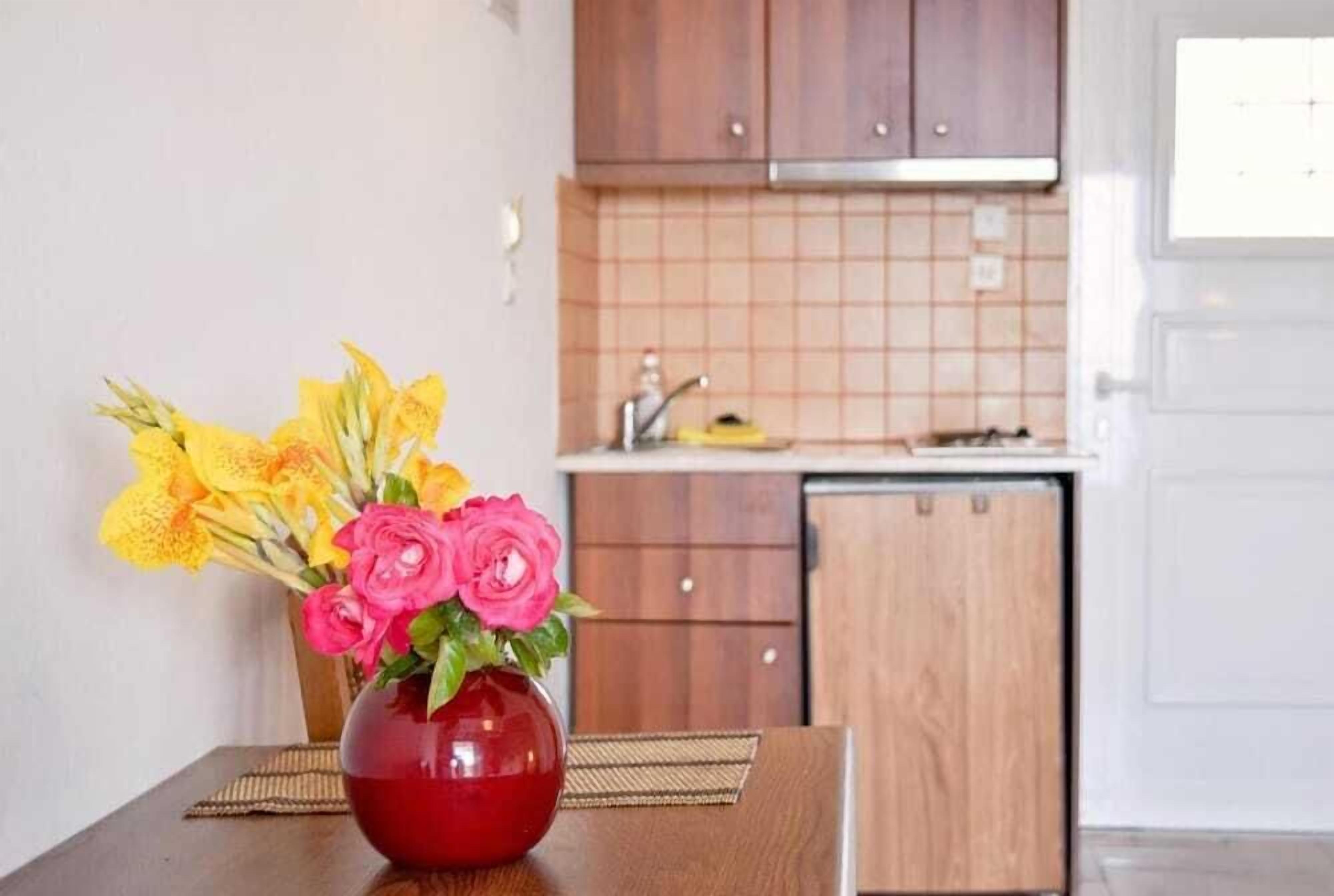 A kitchen with wooden cabinets, a tiled backsplash, and a red vase with flowers on a table.