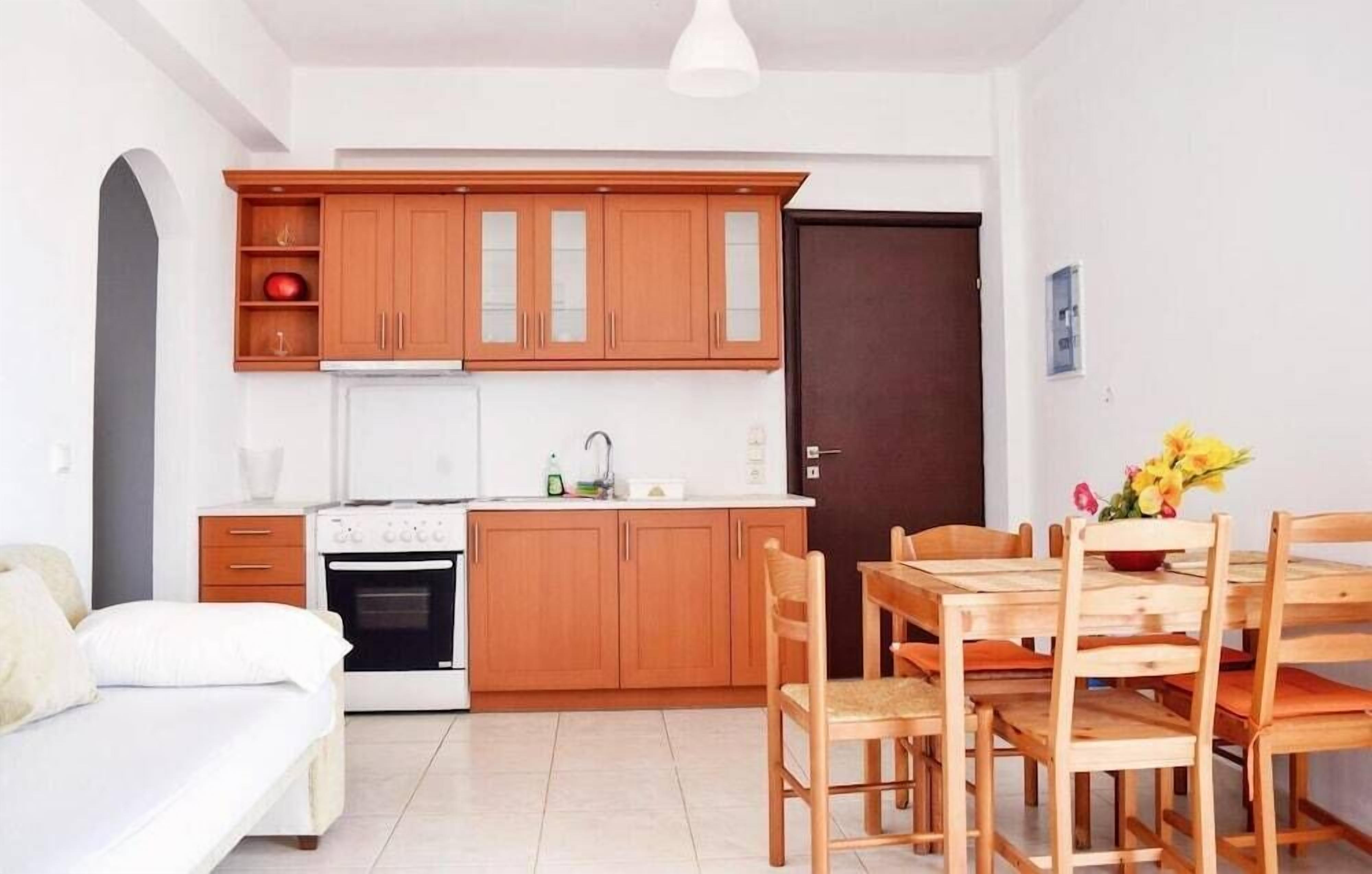 A compact kitchen with wooden cabinets, a white countertop, and a dining area with wooden chairs.
