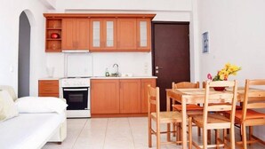 A compact kitchen with wooden cabinets, a white countertop, and a dining area with wooden chairs.