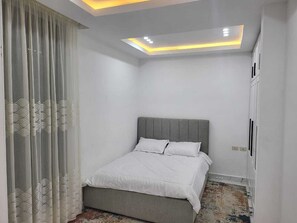 Une chambre à coucher avec un lit, un luminaire au plafond et une fenêtre avec des rideaux.