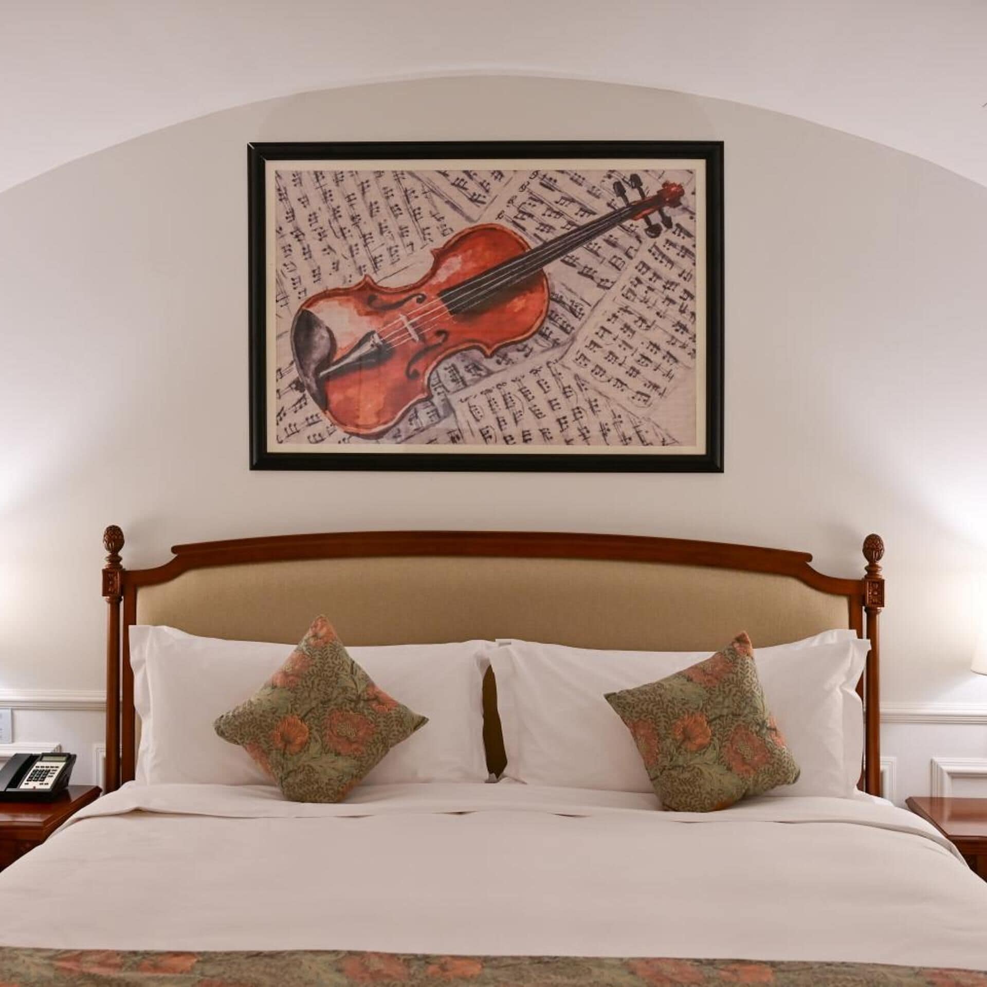 A bed with a wooden headboard, two floral pillows, and a framed picture of a violin on the wall above.