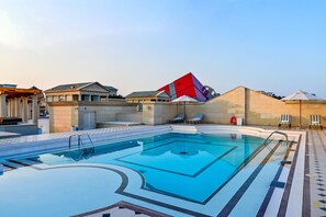 A swimming pool with a geometric tile design, lounge chairs, and a red and blue building in the background. - 21 High Street Residence (Doha)