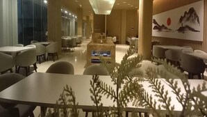 A modern dining area with tables and chairs, a central seating area, and a large painting on the wall. - LK Hotel Chadstone Cikarang (Cikarang)