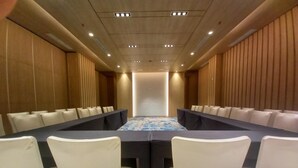 A conference room with a long table, white chairs, and wooden paneling on the walls. - LK Hotel Chadstone Cikarang (Cikarang)