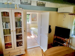 Ein Zimmer mit Bücherregal, einem Bett, einem Fernseher und einer Klimaanlage.