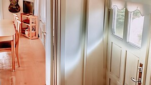 Een kamer met een houten bankje, een deur met een raam, een gitaar en een televisie op een standaard.