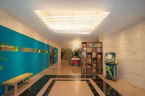 A brightly lit hallway with a blue wall, a wooden bench, a colorful wall art, a toy display, and a trash bin. - Far East Village Hotel Osaka, Honmachi (Osaka)