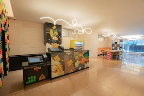 A reception area with a counter featuring cartoon characters, a seating area with a table and chairs, and a large window providing natural light. - Far East Village Hotel Osaka, Honmachi (Osaka)