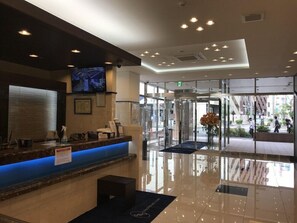 En hotellreception med en blåupplyst disk, en väggmonterad tv och en entré med glasväggar och en karuselldörr.
