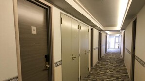 Ein Hotelgang mit Teppichböden, Türen auf beiden Seiten und einem Blick in ein Zimmer am Ende.