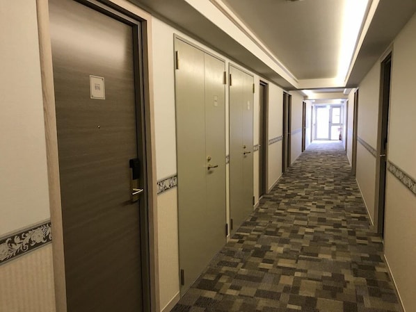 Un couloir d’hôtel avec des planchers recouverts de moquette, des portes des deux côtés et, au bout, une vue sur une autre pièce.
