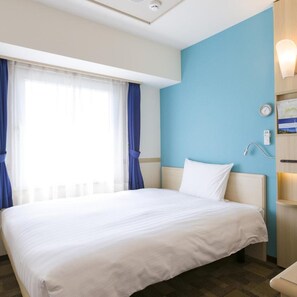 Une chambre d’hôtel avec un lit, une fenêtre avec des rideaux, une horloge murale et une table de chevet avec une lampe.