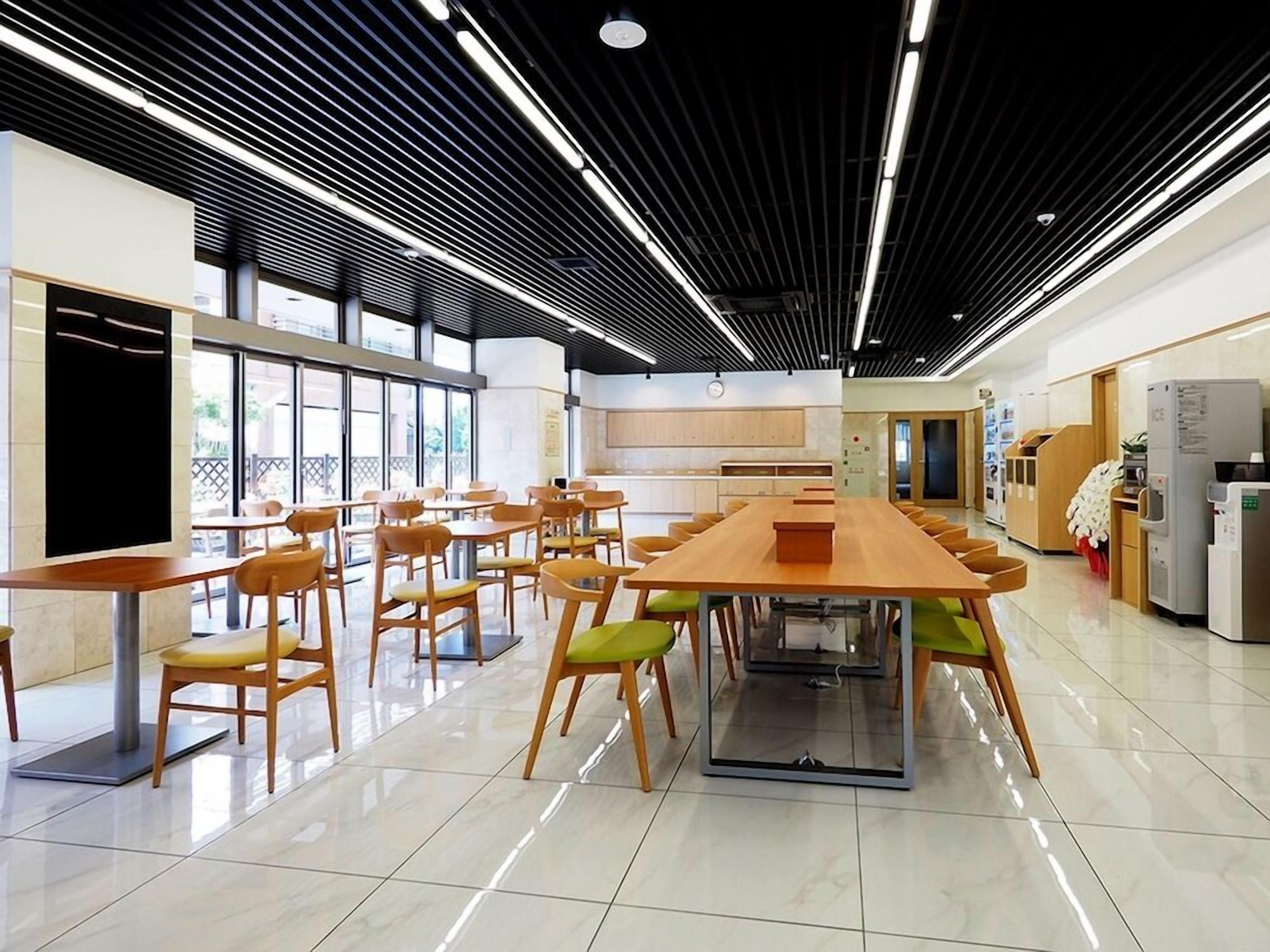 A spacious dining area with a long table and chairs, a kitchen area with appliances, and large windows allowing natural light.