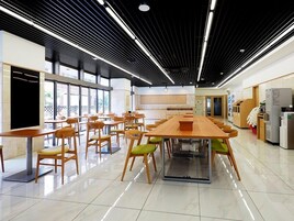 Un comedor amplio con una mesa larga y sillas, una zona de cocina con electrodomésticos, y ventanas grandes que dejan entrar luz natural.