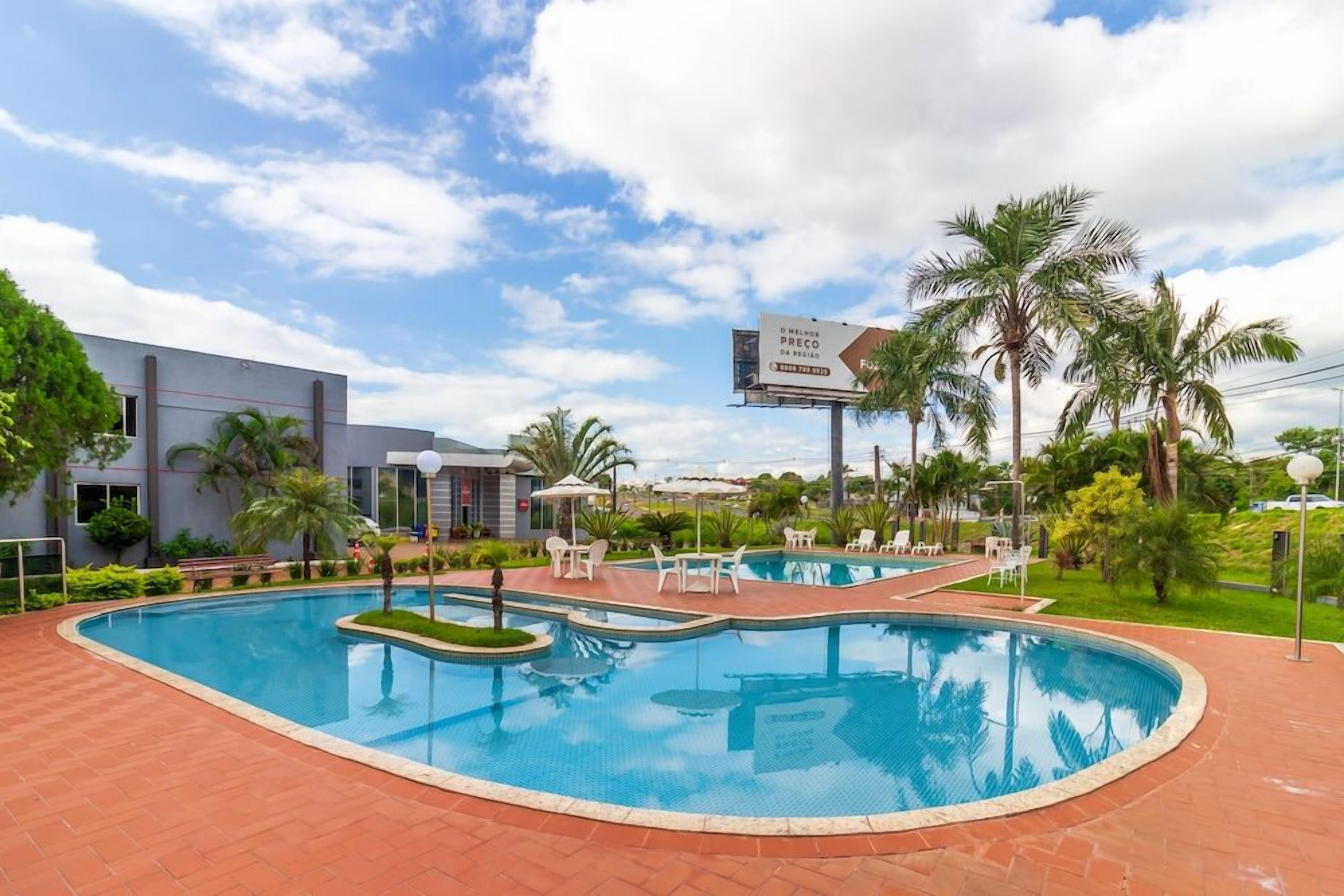 Una piscina con sillas de descanso y palmeras, rodeada por un edificio con un anuncio.