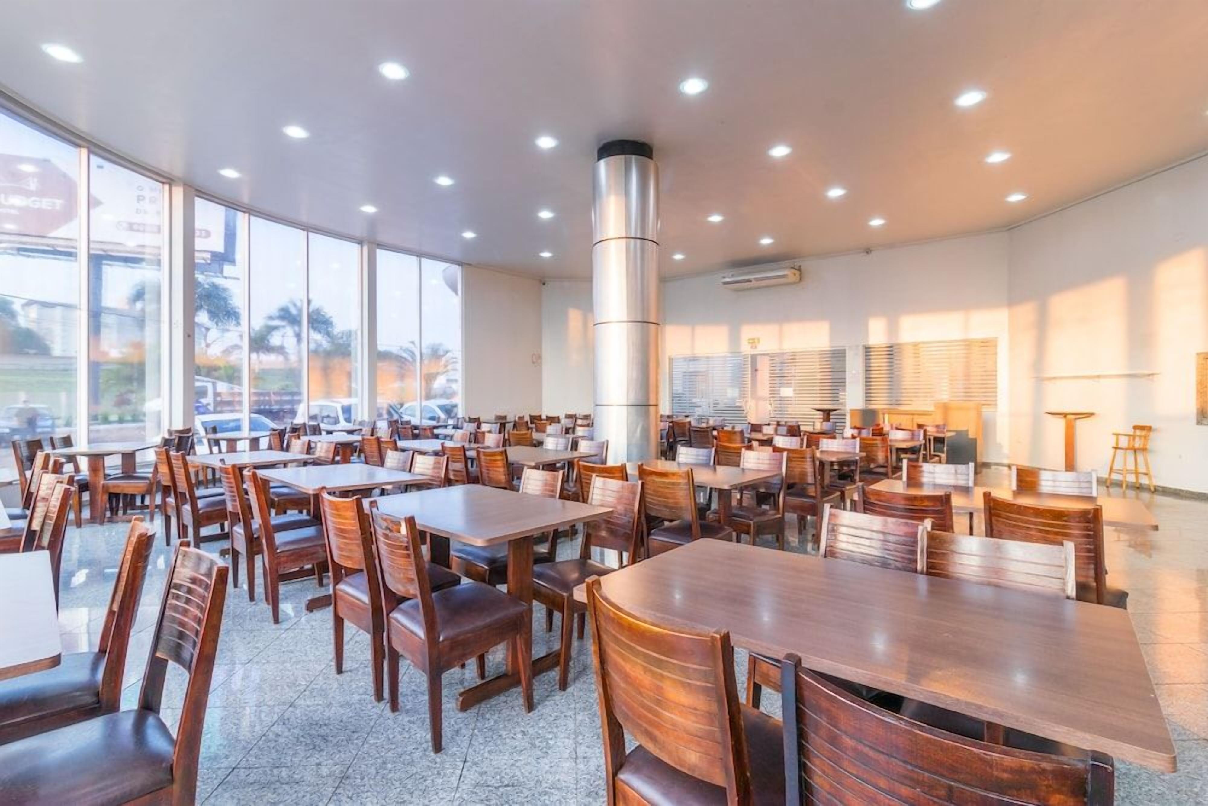 Un comedor amplio e interior con varias mesas y sillas, ventanas grandes y un pilar central.