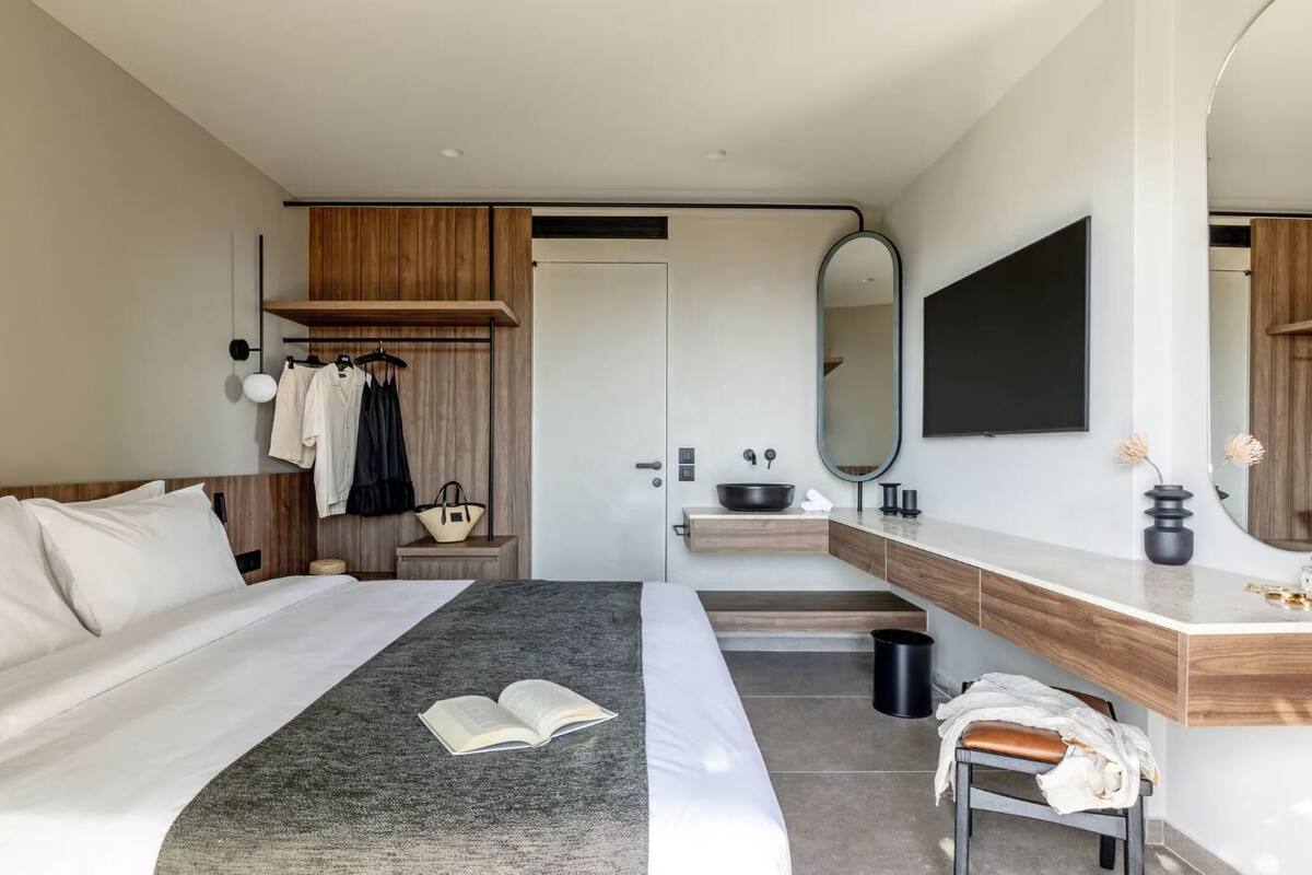 A modern hotel room with a bed, bedside table, mirror, and a vanity with a sink.