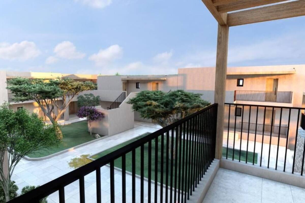 A residential building with a balcony, a small garden, and a clear sky.