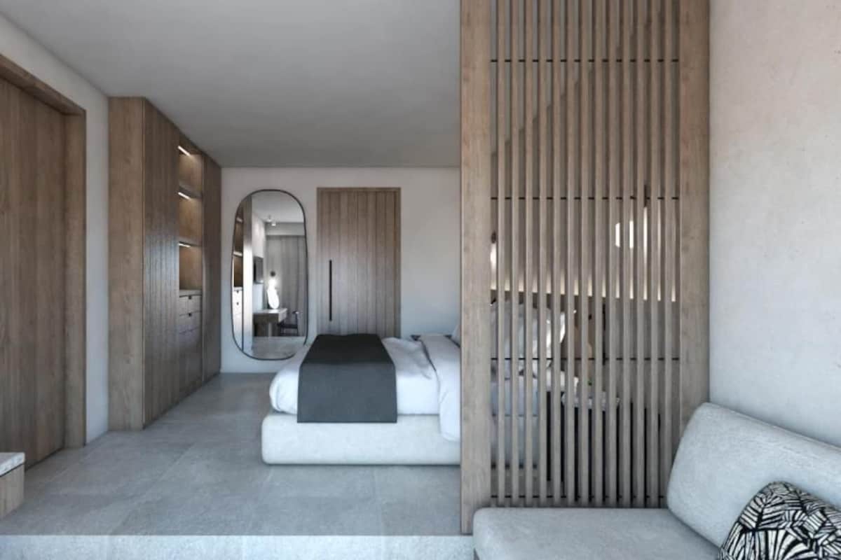 A modern hotel room with a bed, a sofa, a mirror, and wooden paneling.