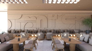 A modern lounge area with sofas, chairs, and tables, featuring a large wall with a geometric design. - Elios Hill (Hersonissos)
