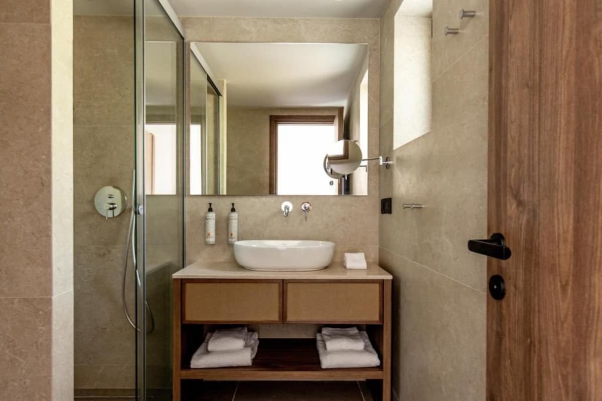A modern bathroom with a glass shower enclosure, a white sink, and a wooden vanity with towels.