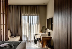 A hotel room with a bed, a desk, a chair, a mirror, and a large window with curtains. - Elios Hill (Hersonissos)