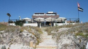 A beachfront hotel with a central building, outdoor seating area with umbrellas, and a flag on a flagpole. - Hotel da Cesare - Maluentu (San Vero Milis)