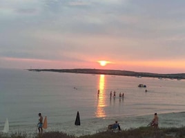 Un atardecer sobre un mar tranquilo con barcos y gente disfrutando en el agua.