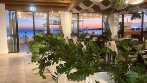 A restaurant with a view of the sunset over the water, featuring a modern interior with white decor and potted plants. - Hotel da Cesare - Maluentu (San Vero Milis)