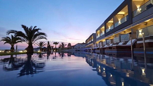 A modern hotel with a reflective pool, palm trees, and a sunset sky. - Sea Coast Resort (Polygyros)
