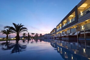 A modern hotel with a reflective pool, palm trees, and a sunset sky. - Sea Coast Resort (Polygyros)