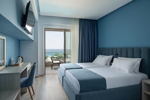 Una habitación de hotel con cama, escritorio, silla, televisor y vista al océano.