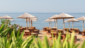 A beach with wooden lounge chairs and thatched umbrellas. - Sea Coast Resort (Polygyros)