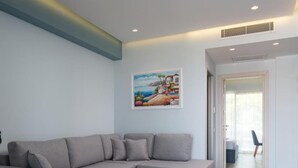 A living room with a grey sectional sofa, a white coffee table, and a painting of a coastal scene. - Sea Coast Resort (Polygyros)